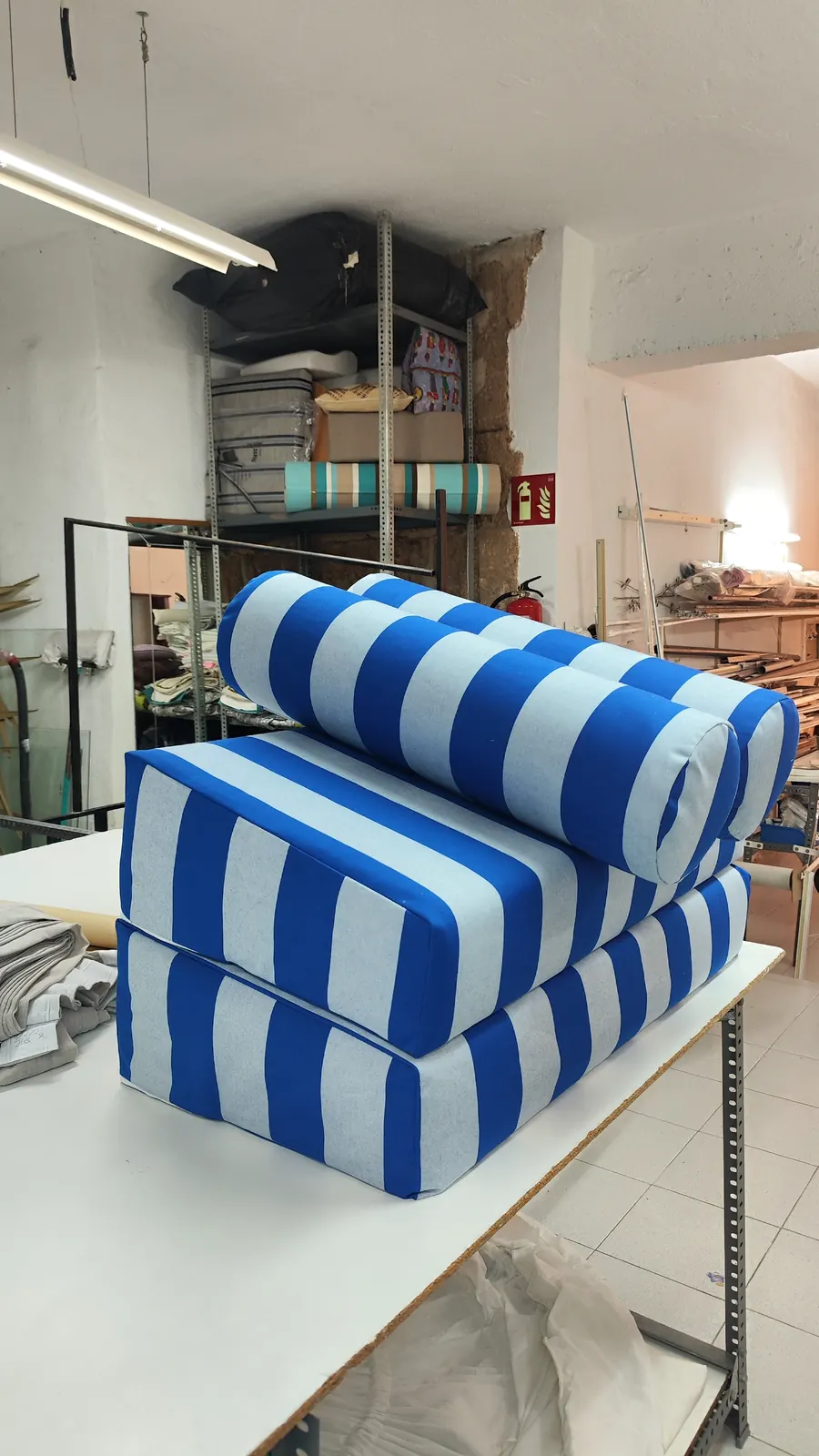 Cojines y colchoneta de rayas azules y blancas apilados en el taller