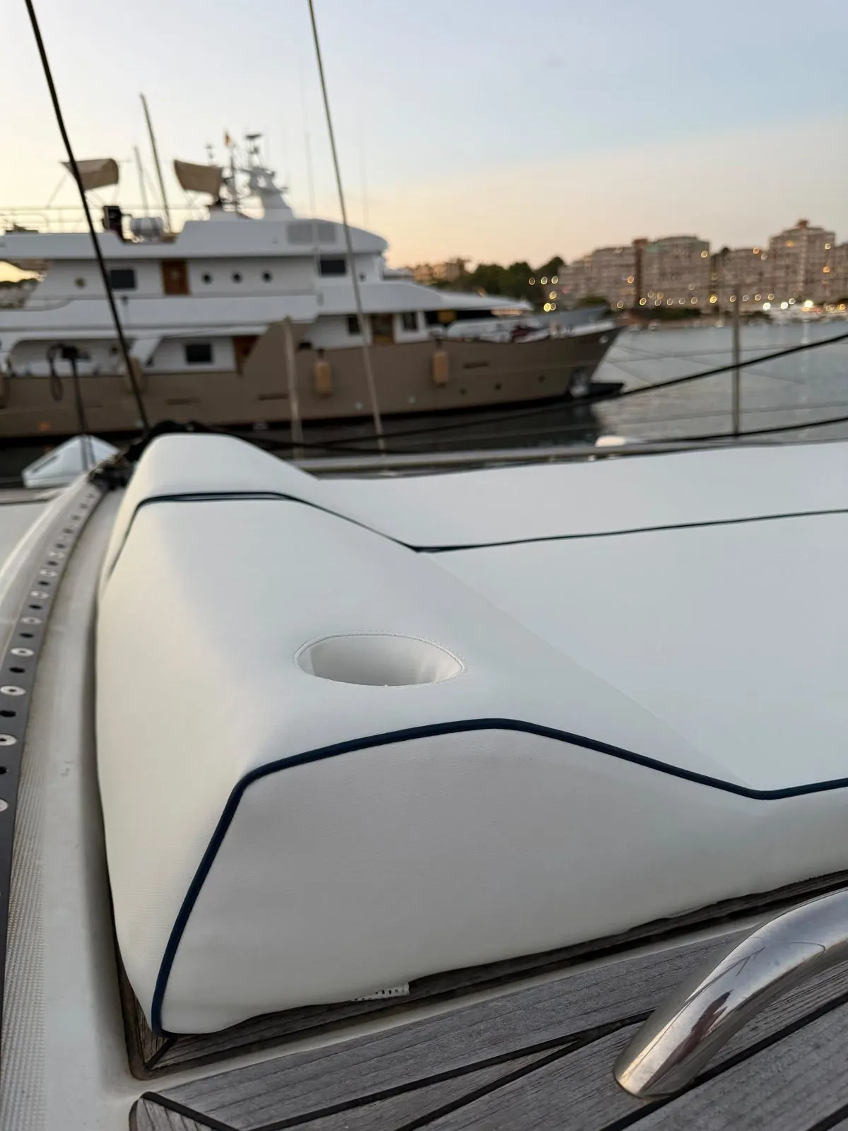 Solárium de proa tapizado en blanco con vivo azul marino y portavasos, con yates al atardecer en Palma